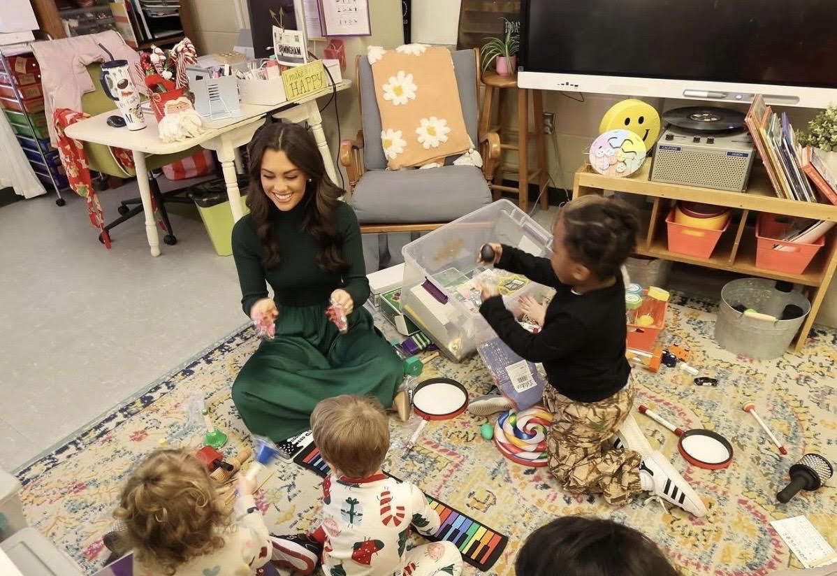 An adult sitting with children during a classroom activity